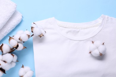 Photo of Cotton branch with fluffy flowers, white t-shirt and terry towel on light blue background, flat lay