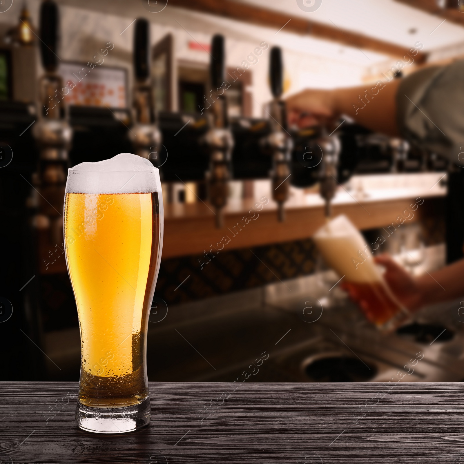 Image of Fresh cold beer on wooden table and bartender in pub, space for text