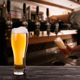 Image of Fresh cold beer on wooden table and bartender in pub, space for text