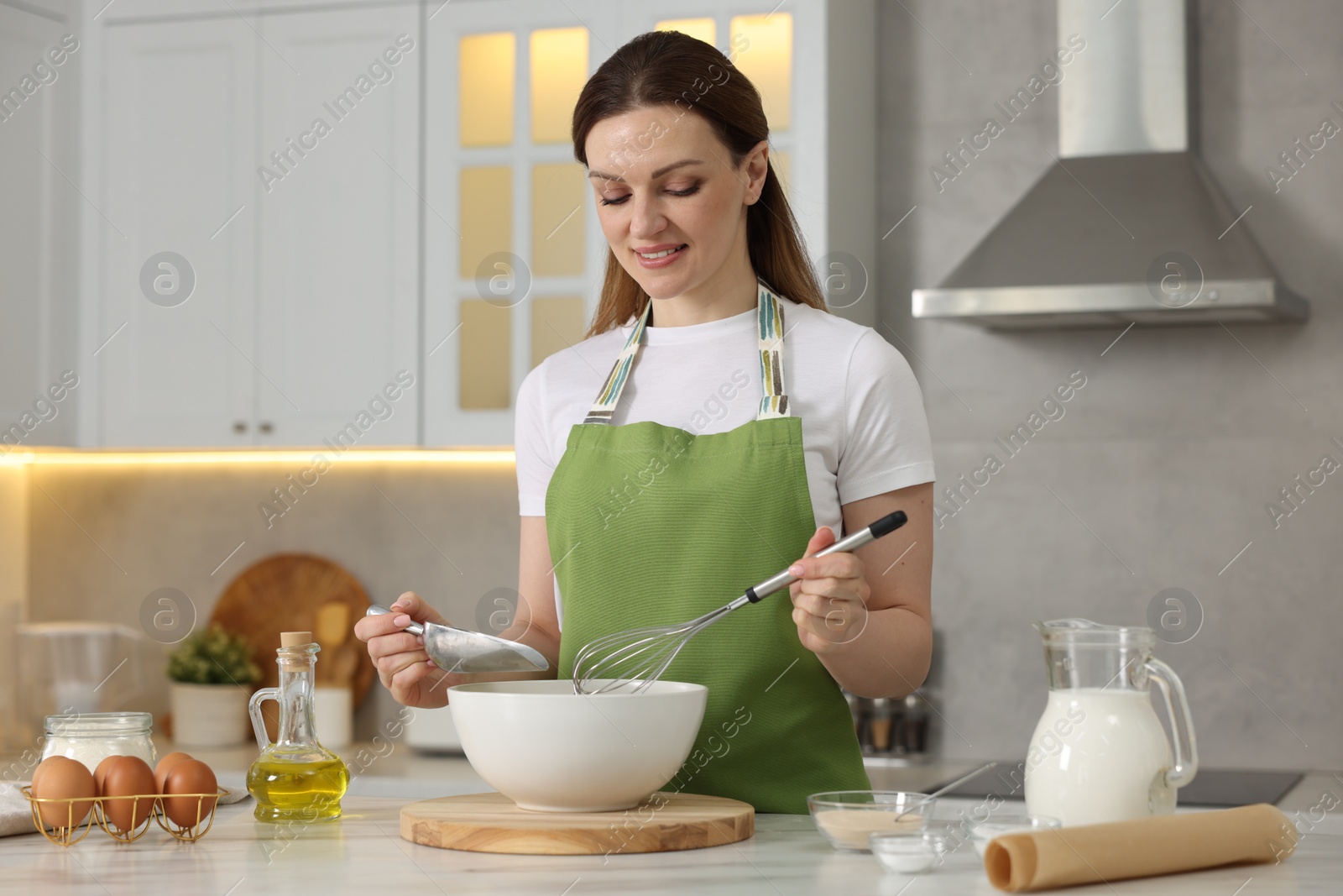 Photo of Making bread. Woman putting flour into bowl at white table in kitchen