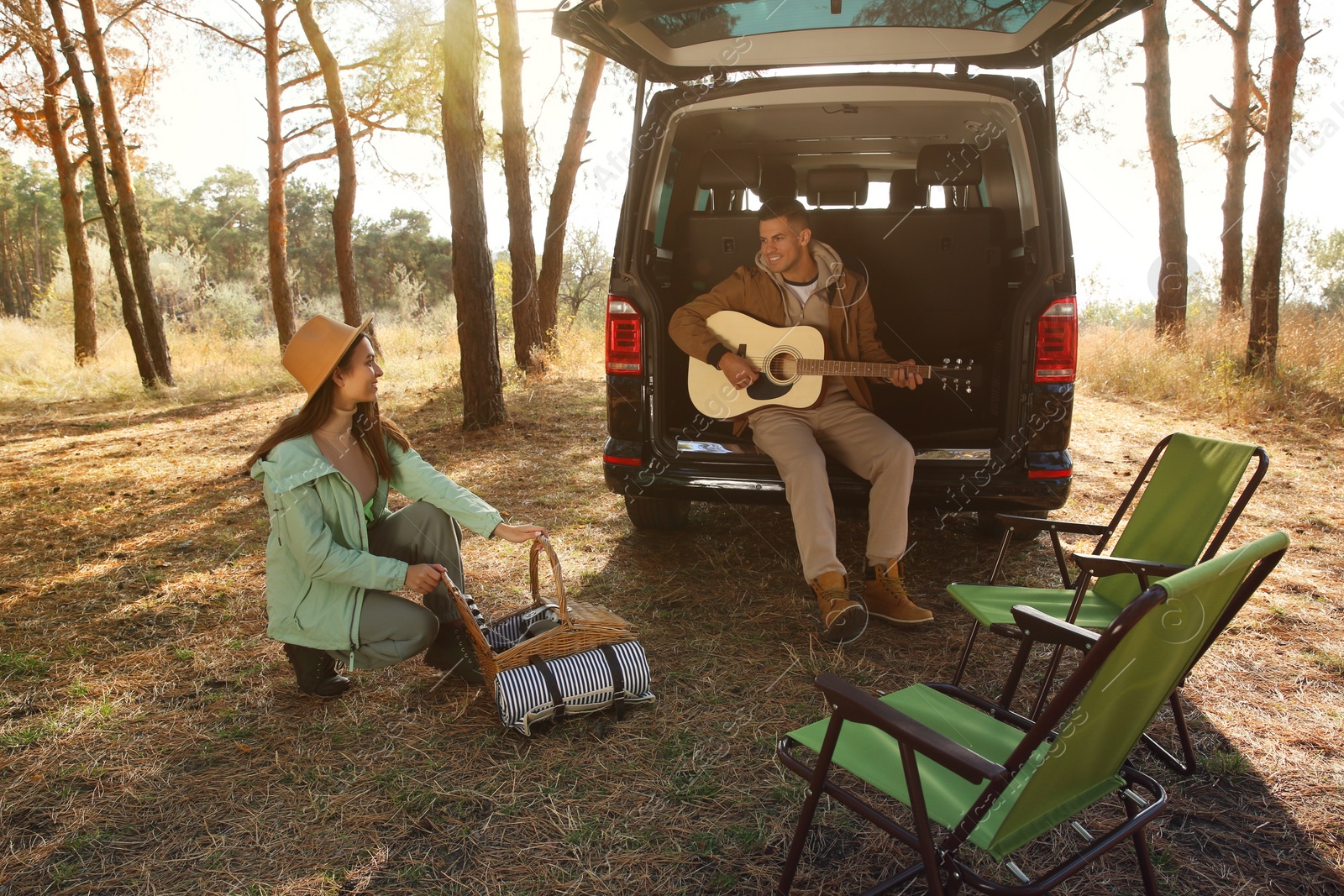 Photo of Couple with guitar, picnic basket and chairs at camping site