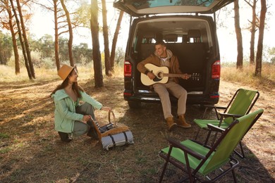 Couple with guitar, picnic basket and chairs at camping site