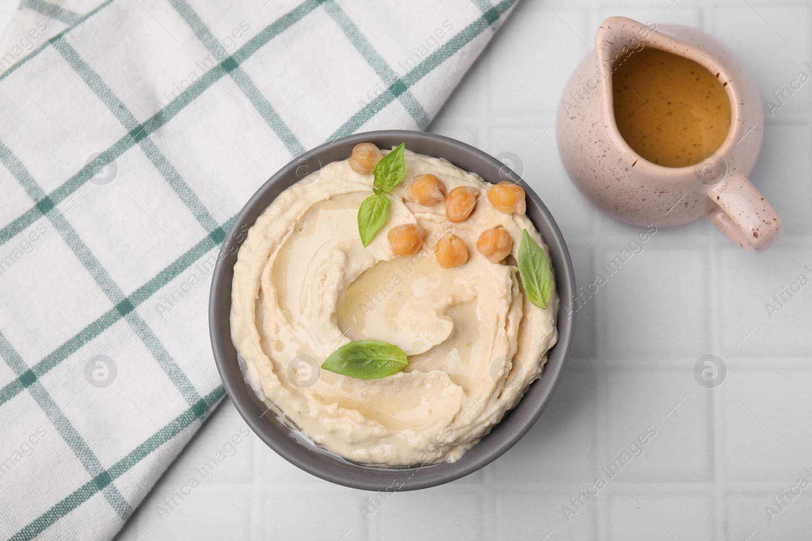 Photo of Delicious hummus with chickpeas served on white tiled table, flat lay