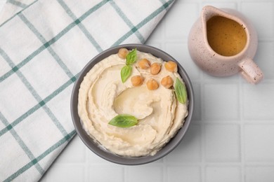 Photo of Delicious hummus with chickpeas served on white tiled table, flat lay