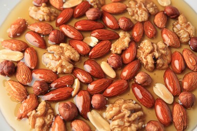 Photo of Different tasty nuts with honey as background, above view