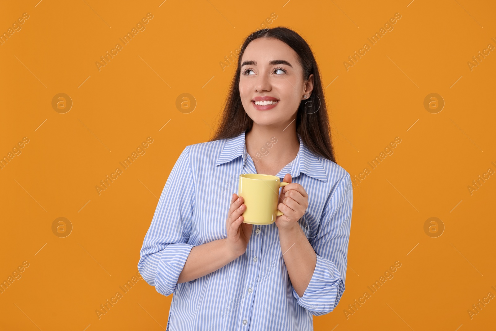 Photo of Happy young woman holding yellow ceramic mug on orange background