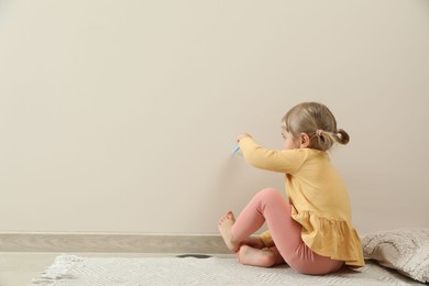 Little girl drawing on beige wall indoors, space for text. Child`s art