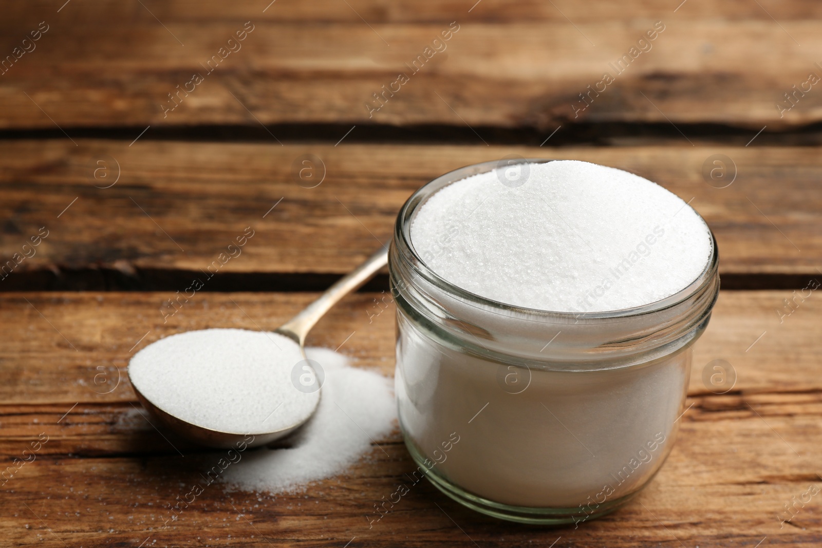 Photo of Glass jar and spoon with salt on wooden table, closeup