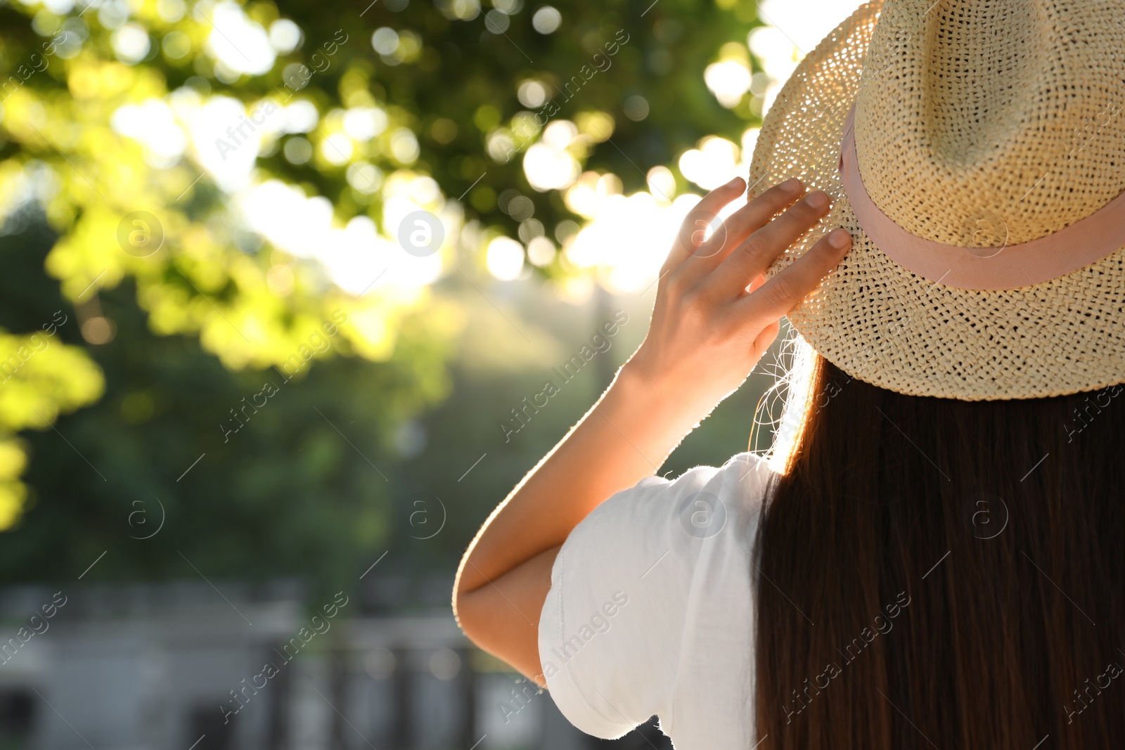 Photo of Young woman in hat outdoors on sunny day, back view