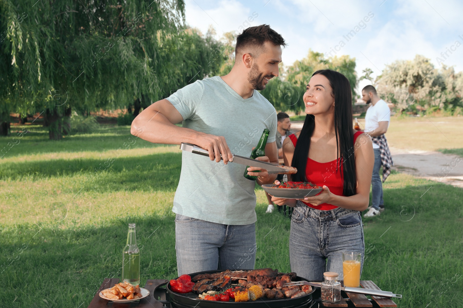 Photo of Happy friends cooking meat and vegetables on barbecue grill in park