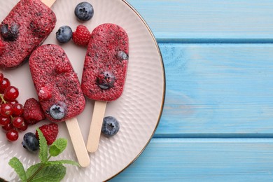Photo of Plate of tasty fruit ice pops with berries on light blue wooden table, top view. Space for text