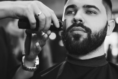 Image of Professional hairdresser working with bearded client in barbershop, closeup. Black and white effect