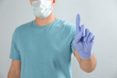 Photo of Man in protective face mask and medical gloves with raised index finger on grey background, closeup