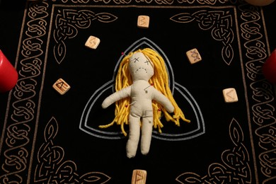 Photo of Voodoo doll pierced with pins and runes on black mat, above view. Curse ceremony