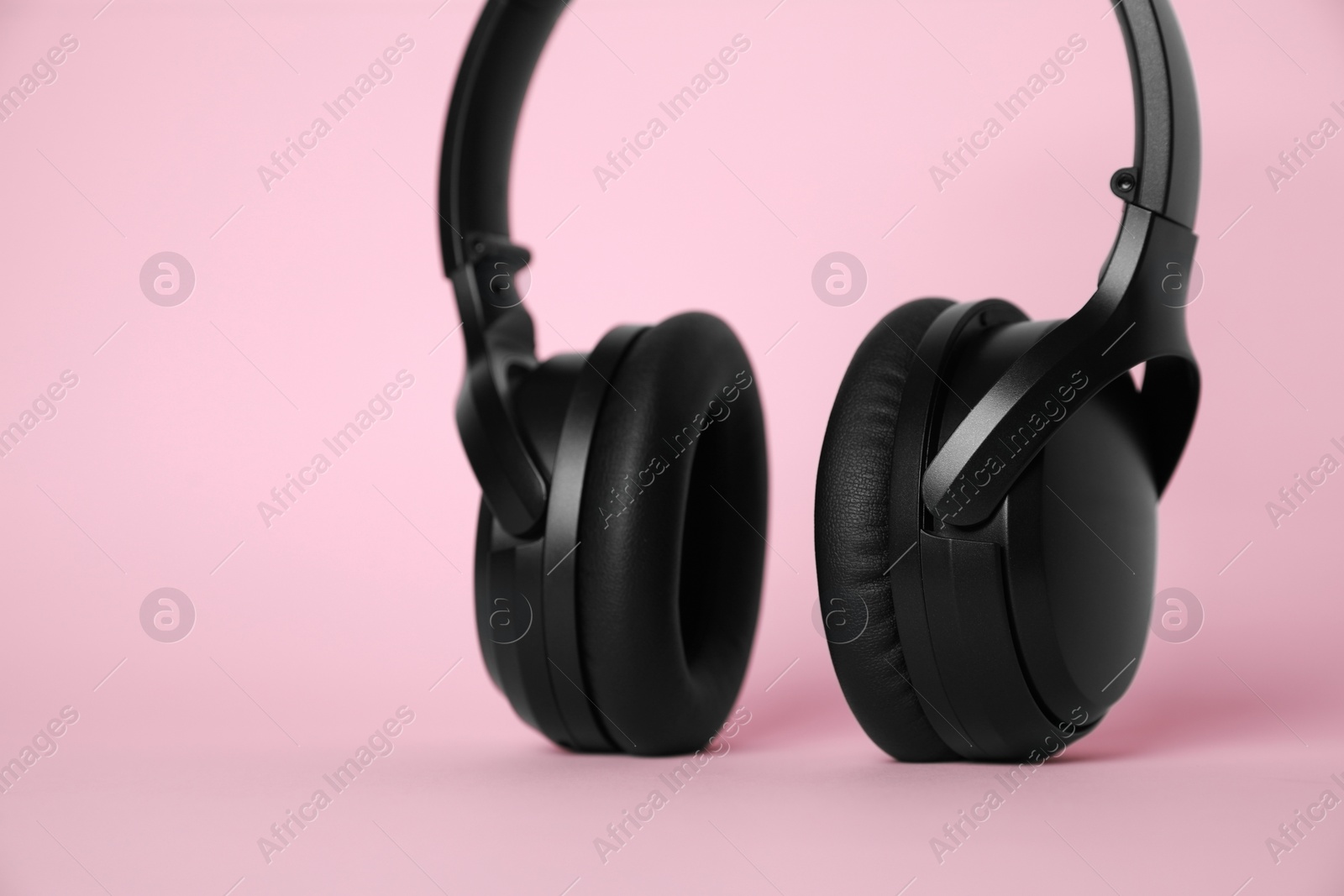 Photo of Modern wireless headphones on pink background, closeup