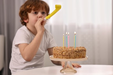 Birthday celebration. Cute boy with party blower at table with tasty cake indoors