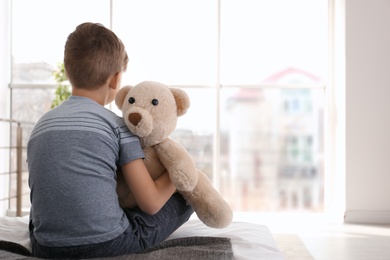 Lonely little boy sitting on bed in room. Autism concept