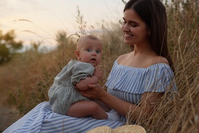 Happy mother with adorable baby in field at sunset