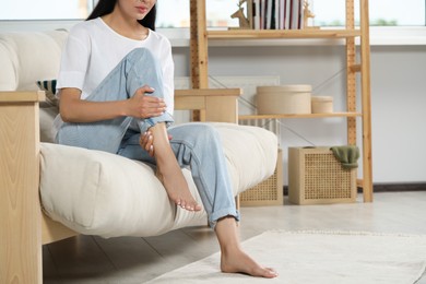 Photo of Young woman rubbing sore leg on sofa at home, closeup