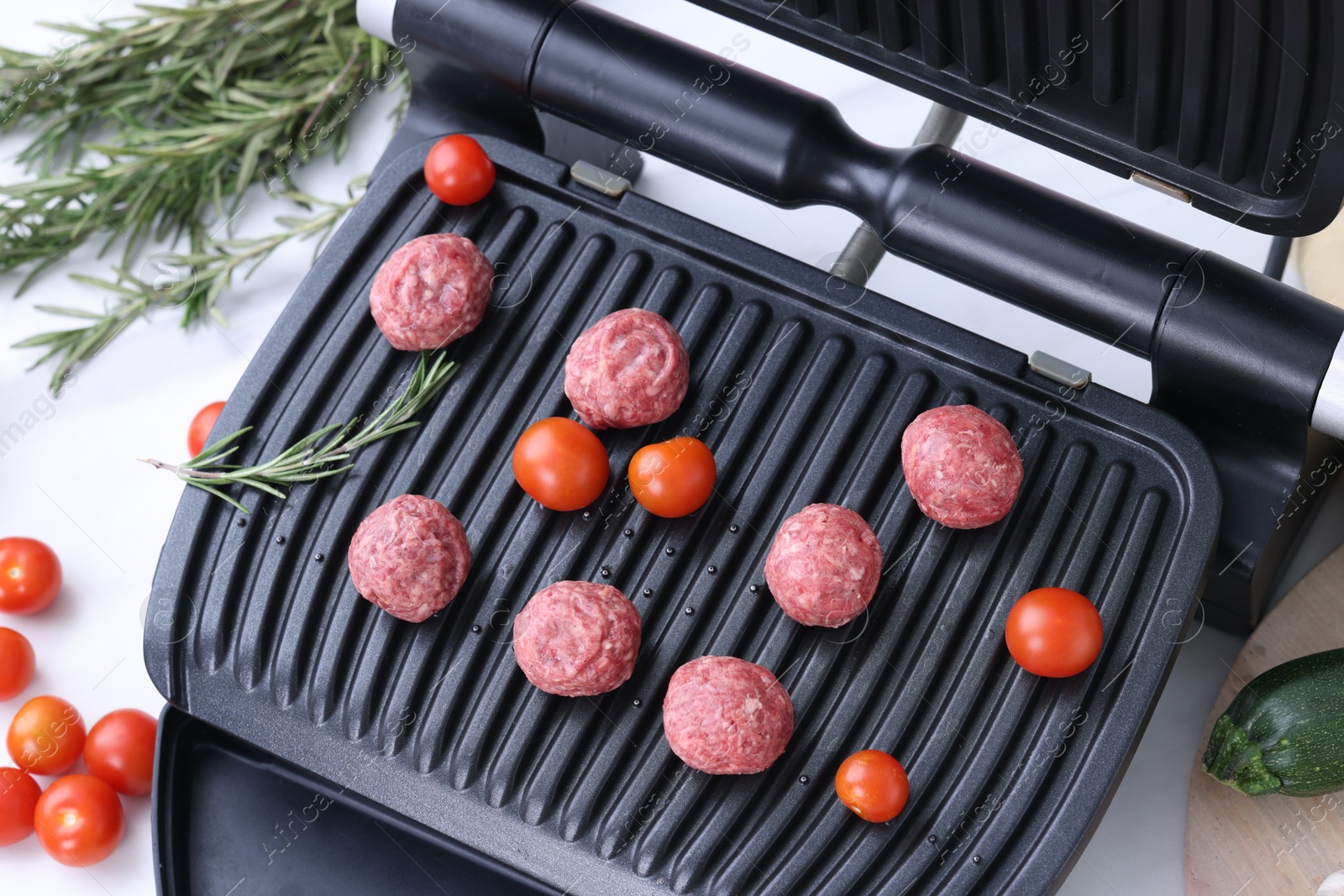 Photo of Electric grill with meatballs, tomatoes and rosemary on white table, above view