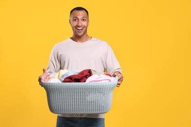 Emotional man with basket full of laundry on orange background. Space for text