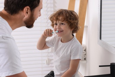 Father and his son brushing teeth together in bathroom