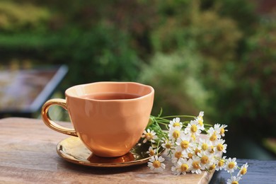 Photo of Cup of delicious chamomile tea and fresh flowers outdoors