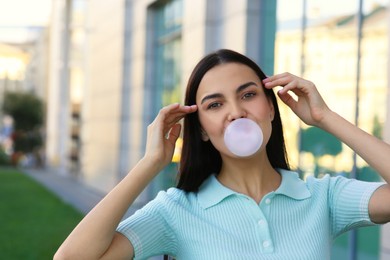 Beautiful woman blowing gum near building outdoors