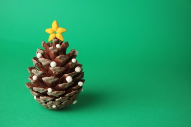 Photo of Christmas tree made from pine cone and plasticine on green background, space for text. Children's handmade ideas