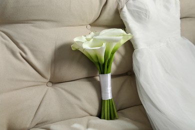 Photo of Beautiful calla lily flowers tied with ribbon and wedding dress on sofa