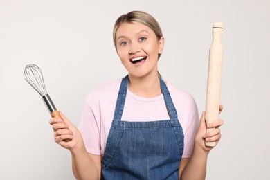 Photo of Beautiful young woman in clean apron with kitchen tools on light grey background