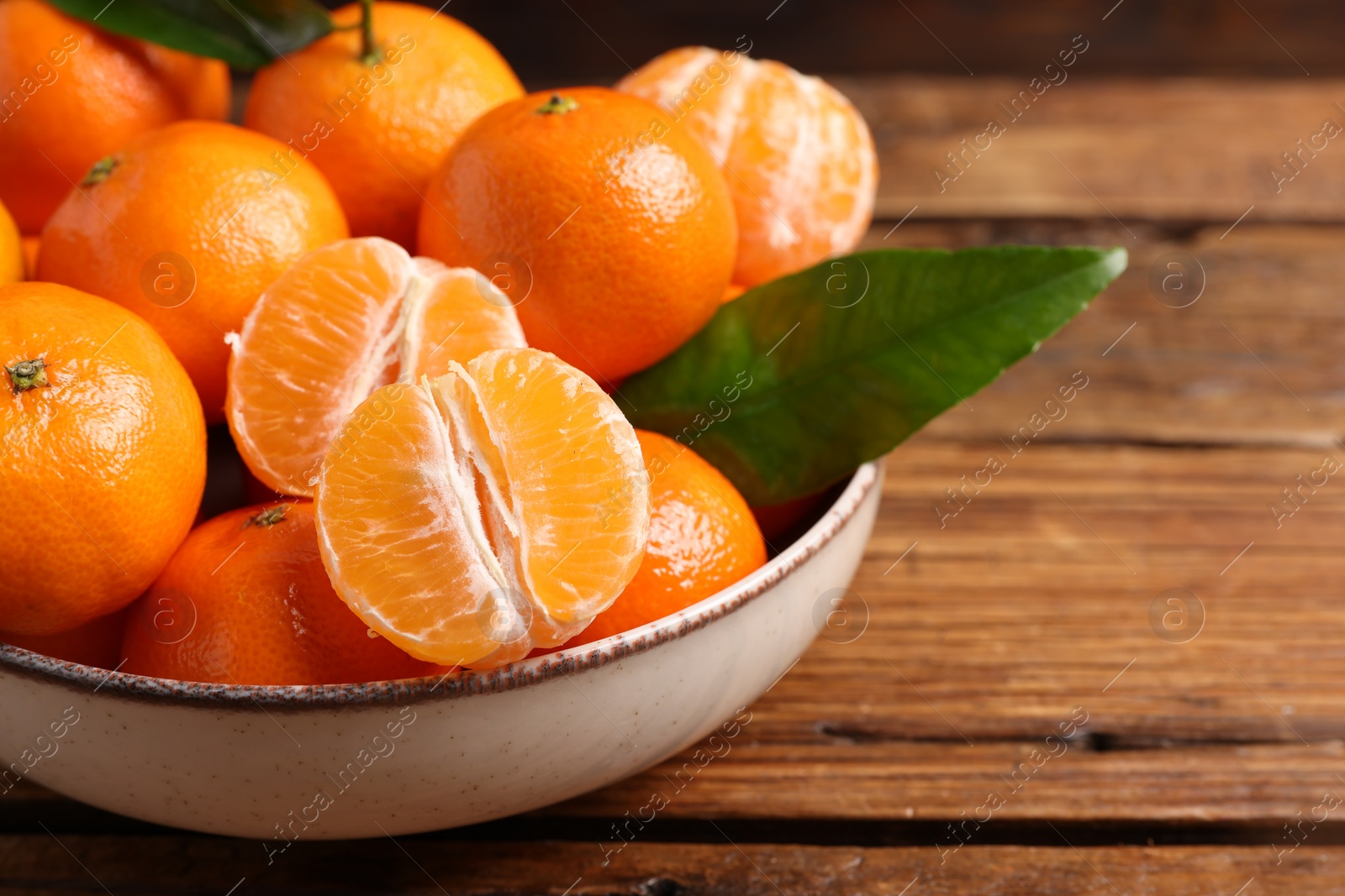 Photo of Fresh tangerines with green leaves in bowl on wooden table, closeup