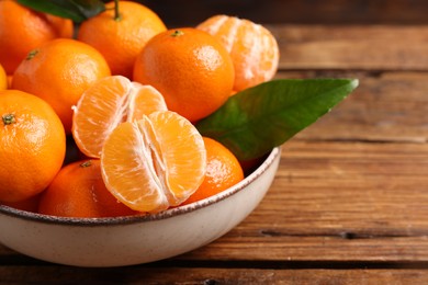 Fresh tangerines with green leaves in bowl on wooden table, closeup