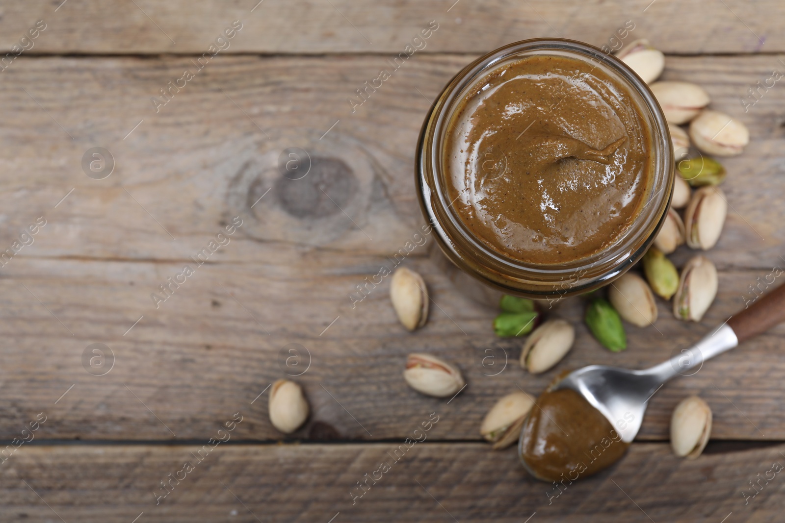 Photo of Tasty pistachio nut paste in jar and spoon on wooden table, flat lay. Space for text