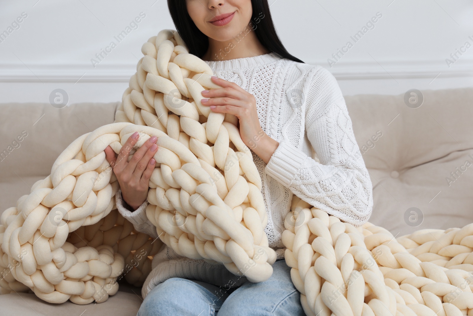 Photo of Woman with chunky knit blanket on sofa at home, closeup