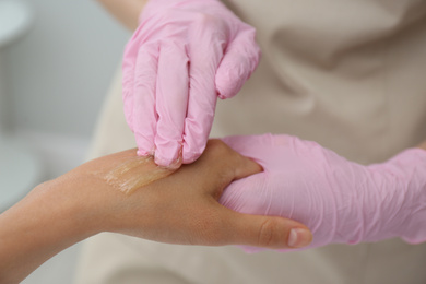 Photo of Woman getting wax epilation of hand in salon, closeup