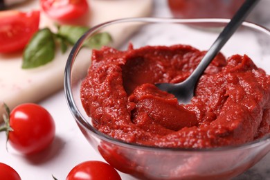 Photo of Glass bowl of tasty tomato paste with spoon and ingredients on white marble table, closeup. Space for text