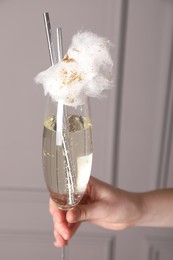 Woman holding glass of cotton candy cocktail near grey wall, closeup