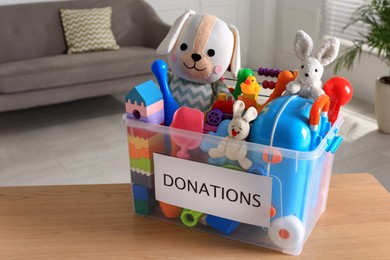 Donation box with different child toys on wooden table at home