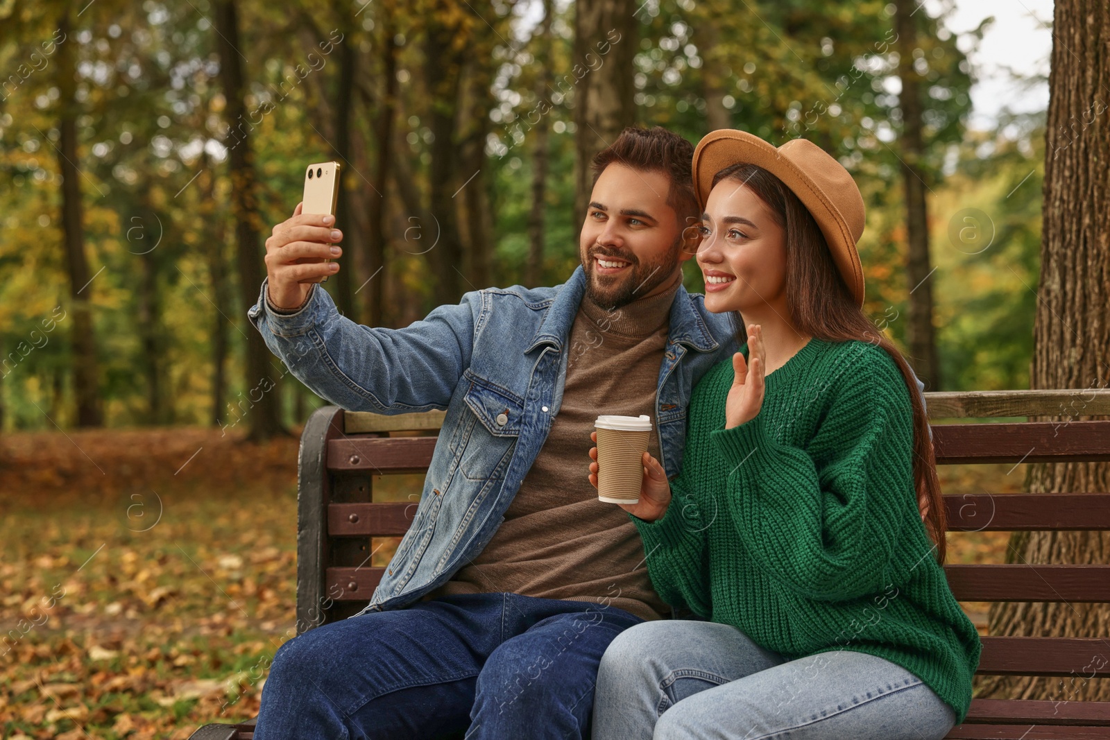 Photo of Happy young couple taking selfie on wooden bench in autumn park