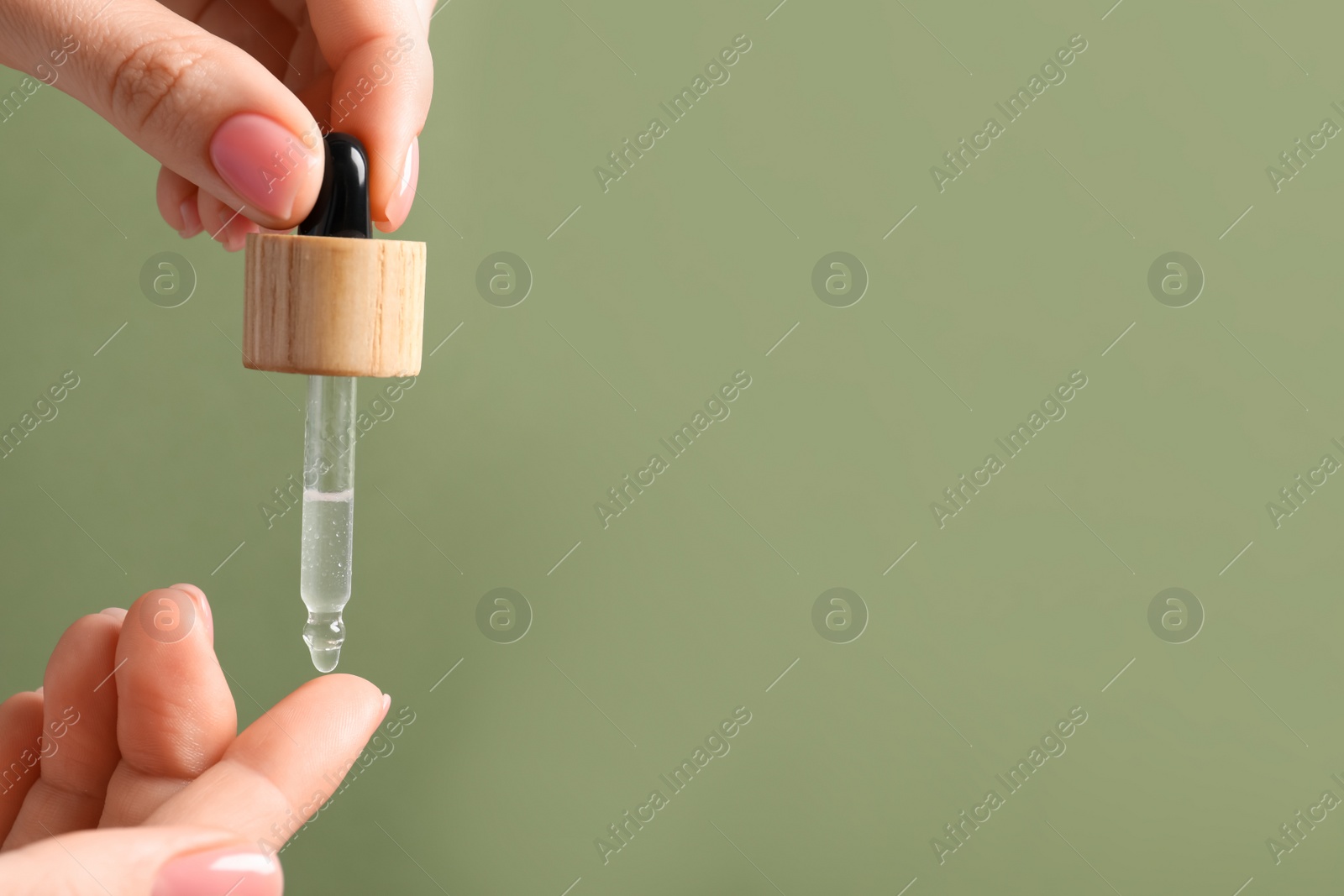 Photo of Woman dripping serum from pipette on her hand against olive background, closeup. Space for text