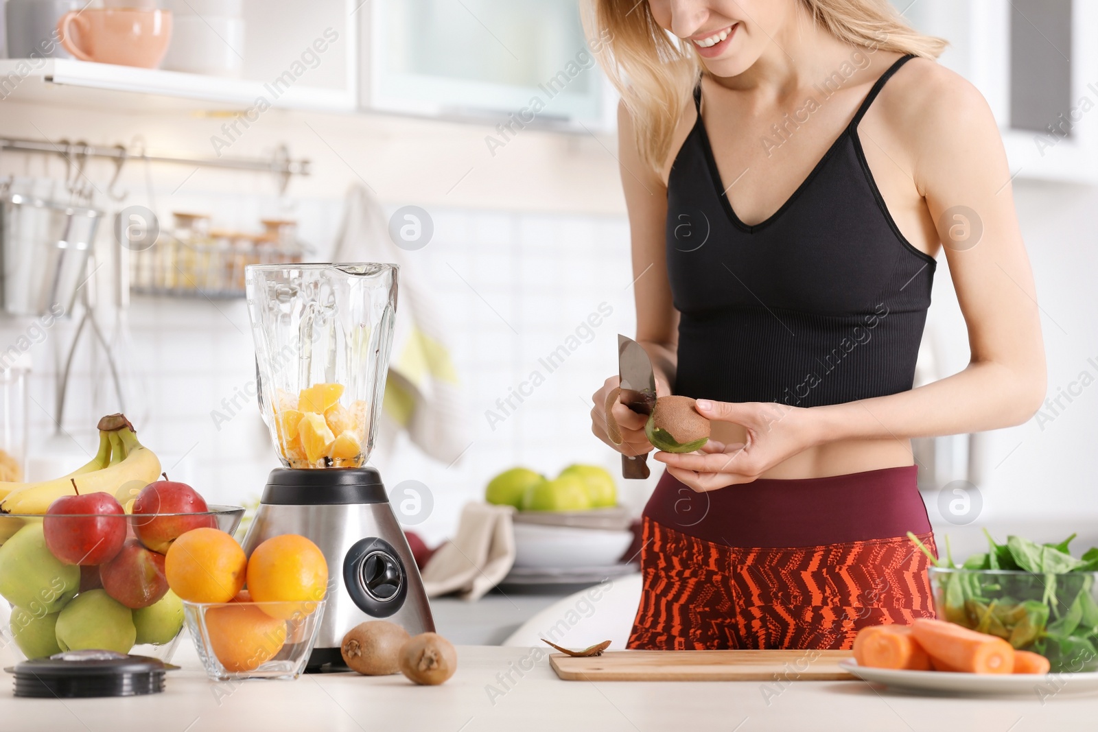 Photo of Young woman preparing tasty healthy smoothie at table in kitchen