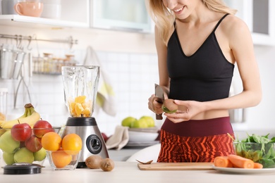 Young woman preparing tasty healthy smoothie at table in kitchen