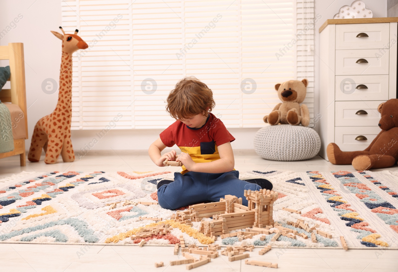 Photo of Little boy playing with wooden construction set on carpet in room. Child's toy