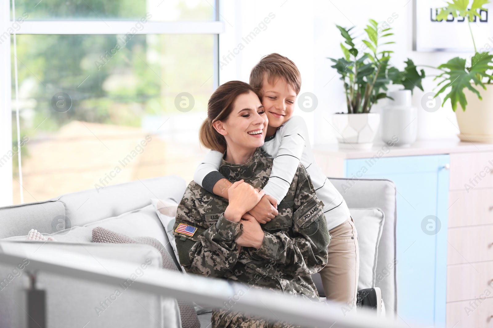 Photo of Woman in military uniform with her little son on sofa at home