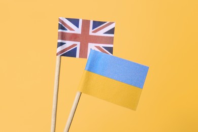 Small paper flags of Ukraine and United Kingdom on orange background, closeup