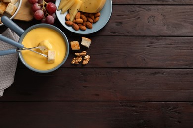 Pot of tasty cheese fondue and snacks on wooden table, flat lay. Space for text