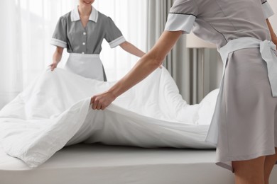 Photo of Professional chambermaids making bed in hotel room, closeup