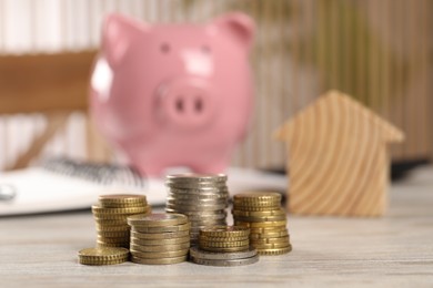 Photo of House model, stacked coins and piggy bank on wooden table, selective focus