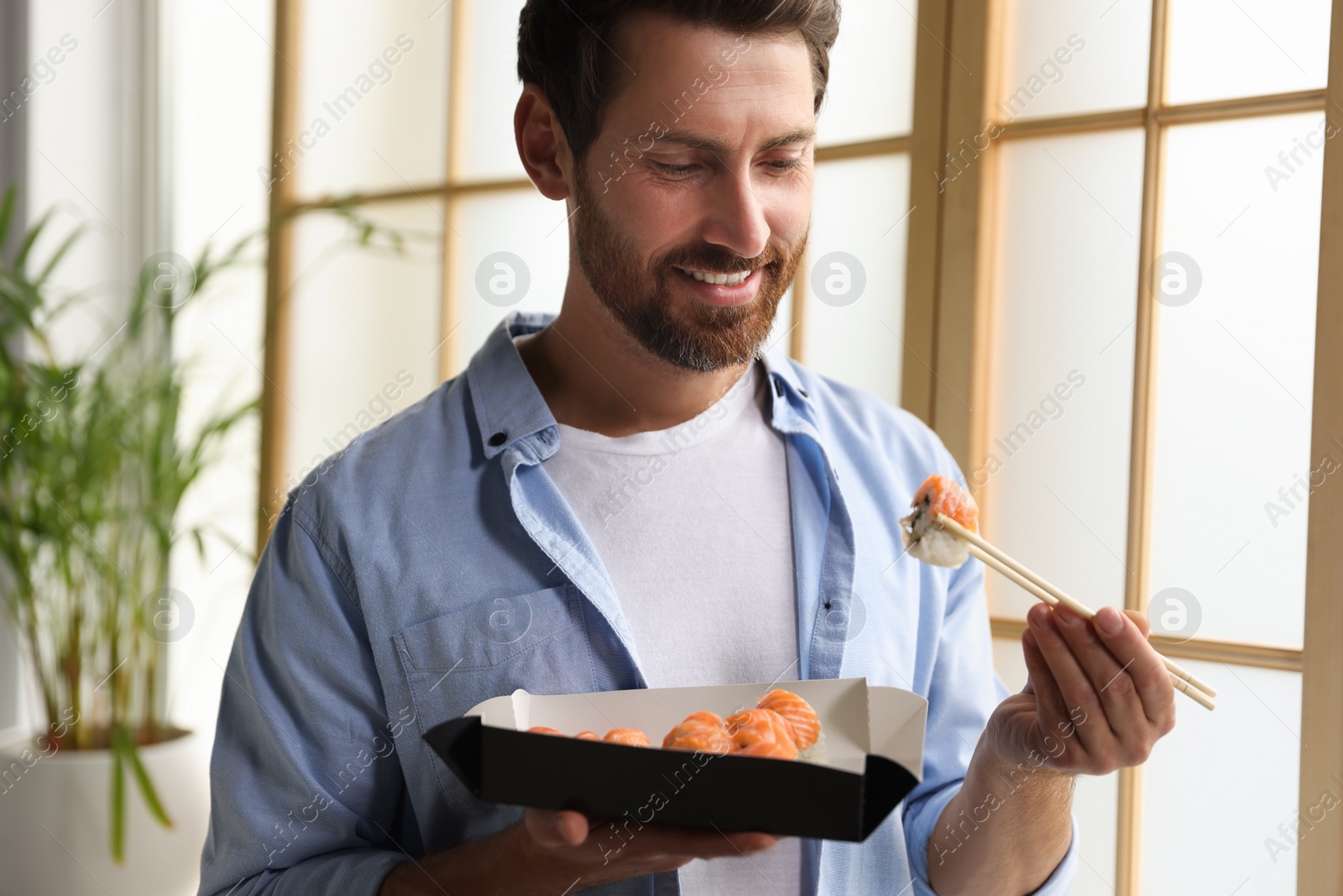 Photo of Handsome man eating sushi rolls with chopsticks indoors